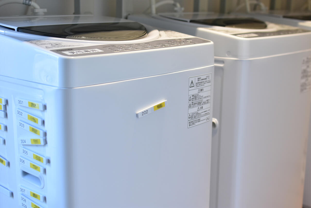 ランドリースペースの様子2。使用中の洗濯機には、自分の名前が入った磁石を表側に貼り付ける仕様とのこと。|1F ランドリー
